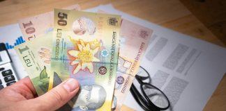 Hand holding Romanian leu banknotes above financial documents, depicting finance and economy.