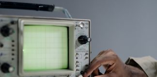 A person adjusts settings on a vintage oscilloscope in a studio environment.