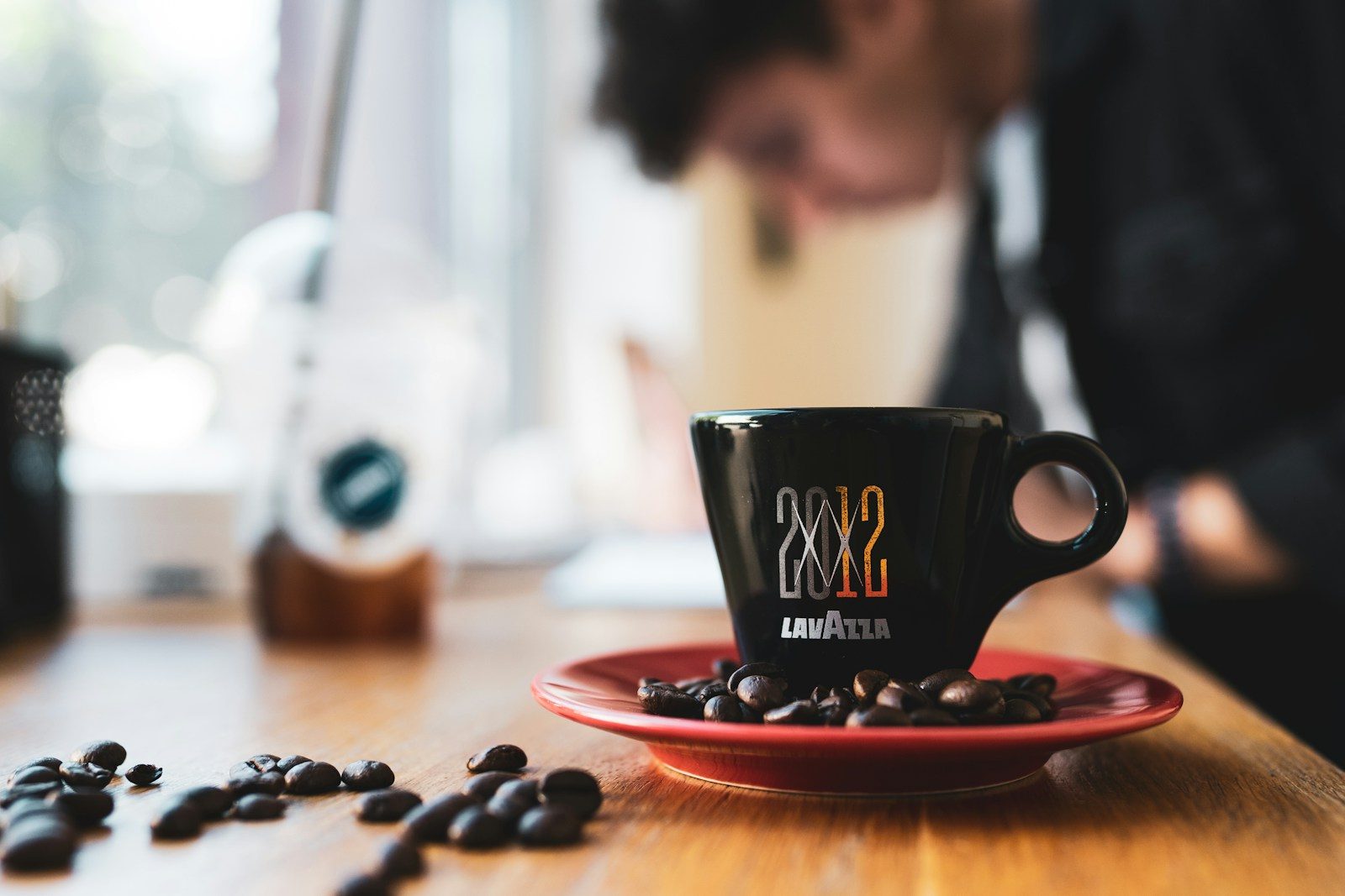 black coffee cup in a red plate with black coffee bean lot close-up photography